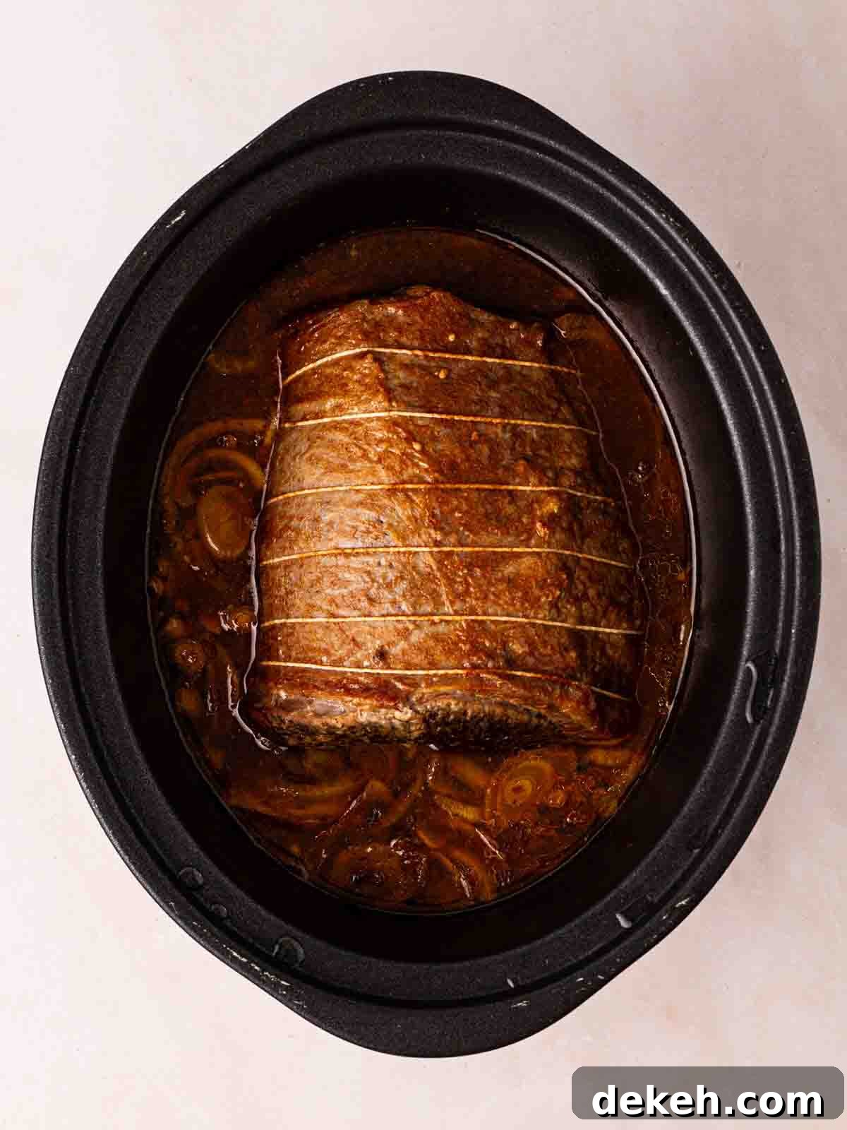 A cooked piece of beef brisket with onions in a slow cooker pan.