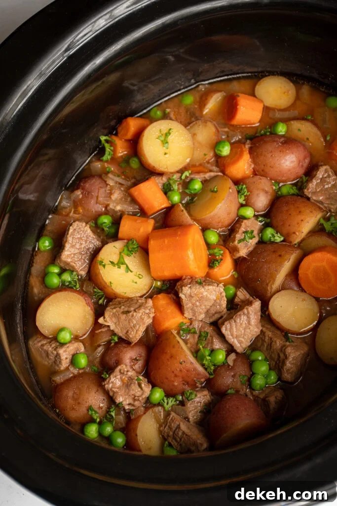 Crockpot full of beef stew filled with carrots, potatoes, chuck roast, and peas.