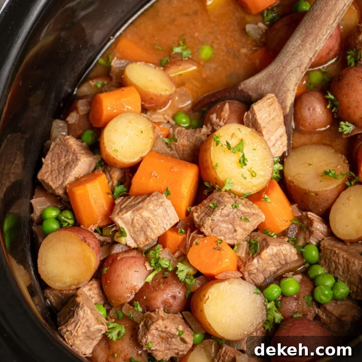 Black crockpot filled with beef stew with big chunks of vegetables and stew meat and a wood spoon scooping them.