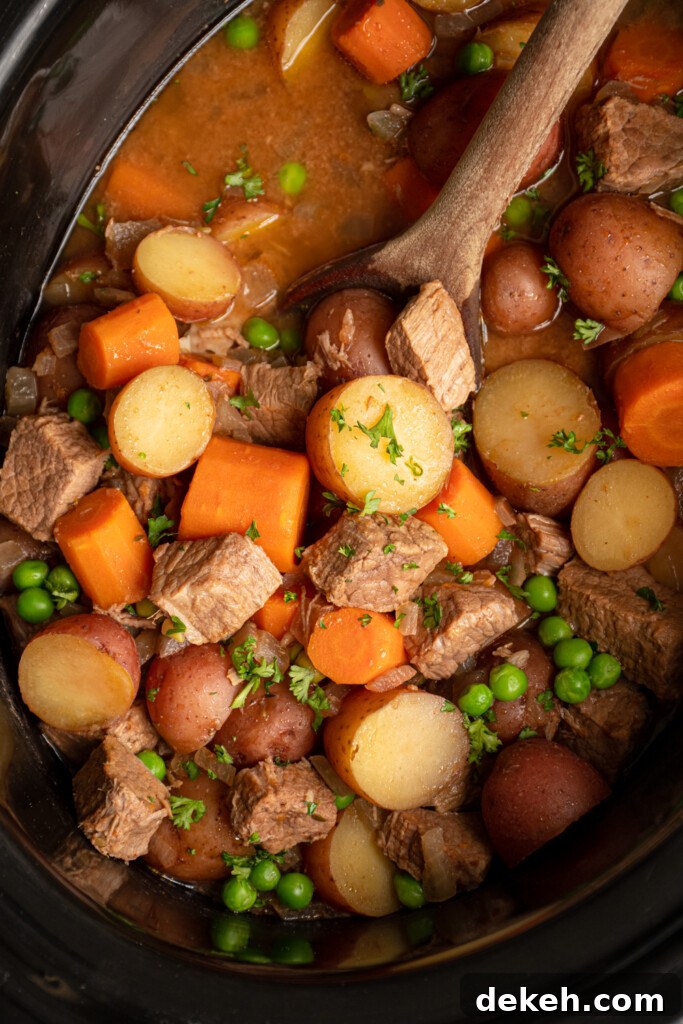 Close up of vegetables and stew meat in the crockpot with a wooden spoon scooping the beef stew.