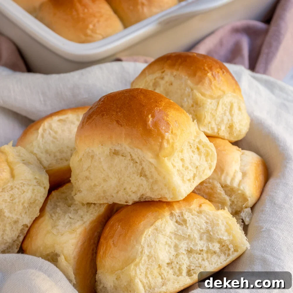 A linen lined basket filled with a bunch of golden brown soft dinner rolls.