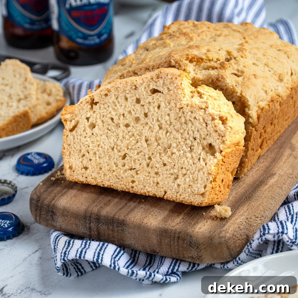 A slice of beer bread on a cutting board propped up against a loaf of easy beer bread.