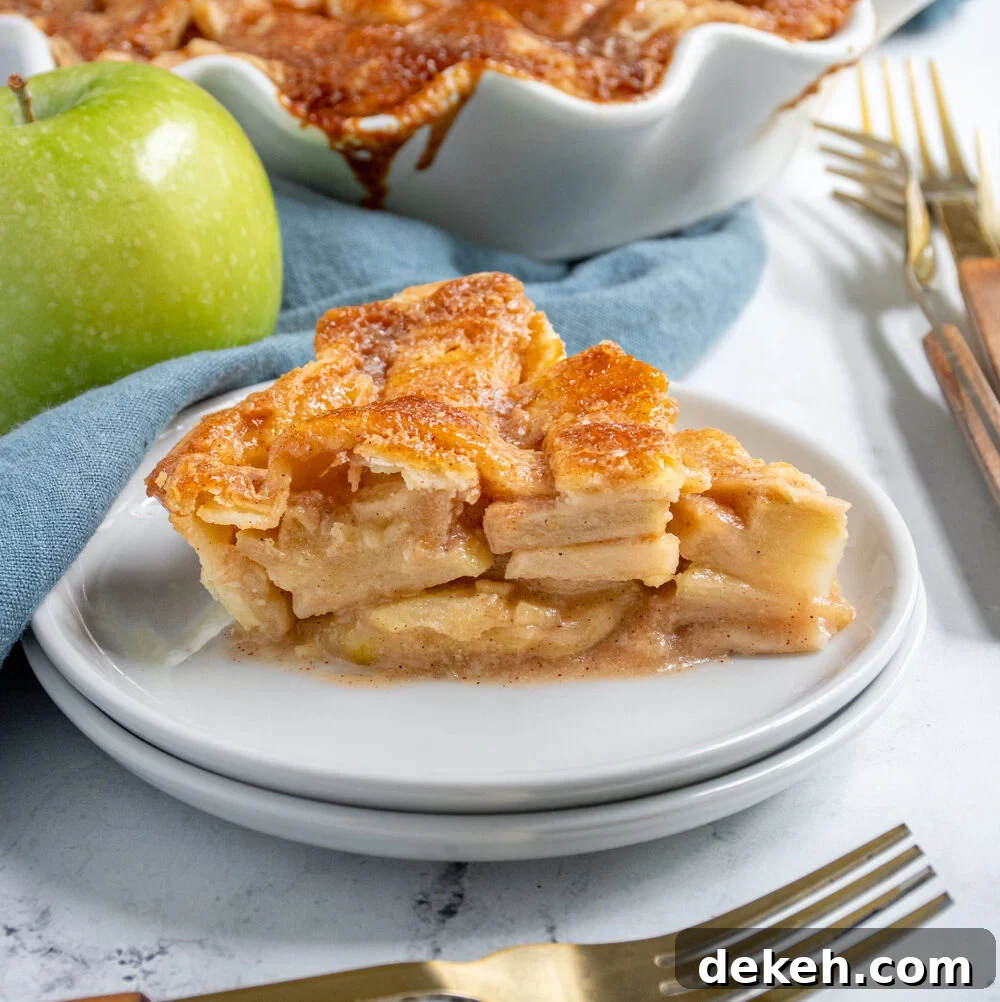 A slice of homemade apple pie on a plate showing of the apple inside and the lattice top.