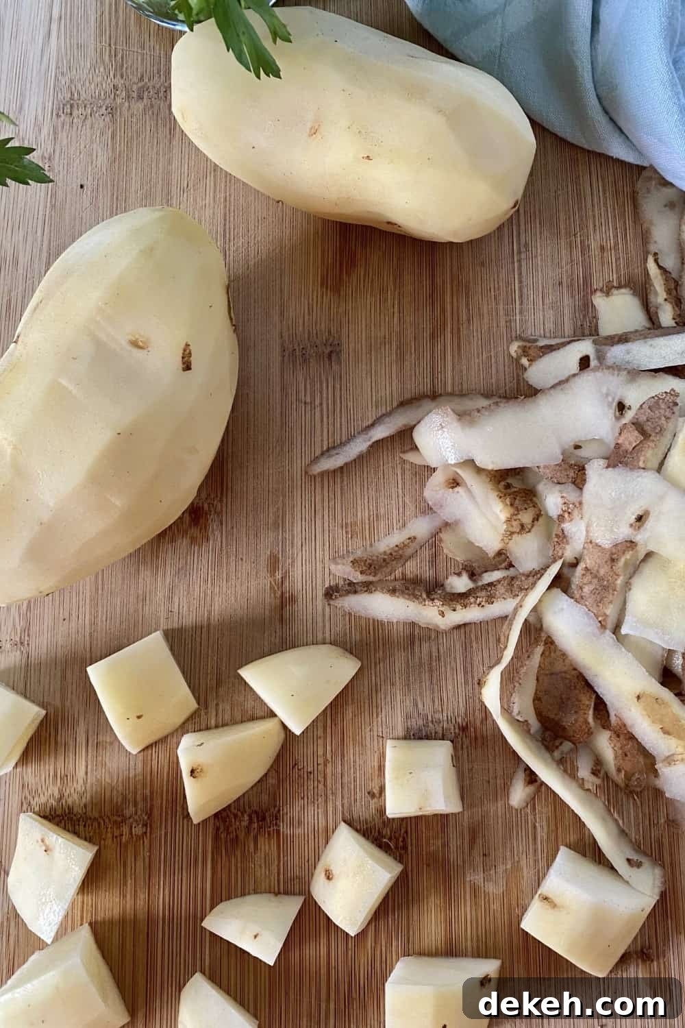 Peeled potatoes, cubed potatoes and potato peels on a cutting board.