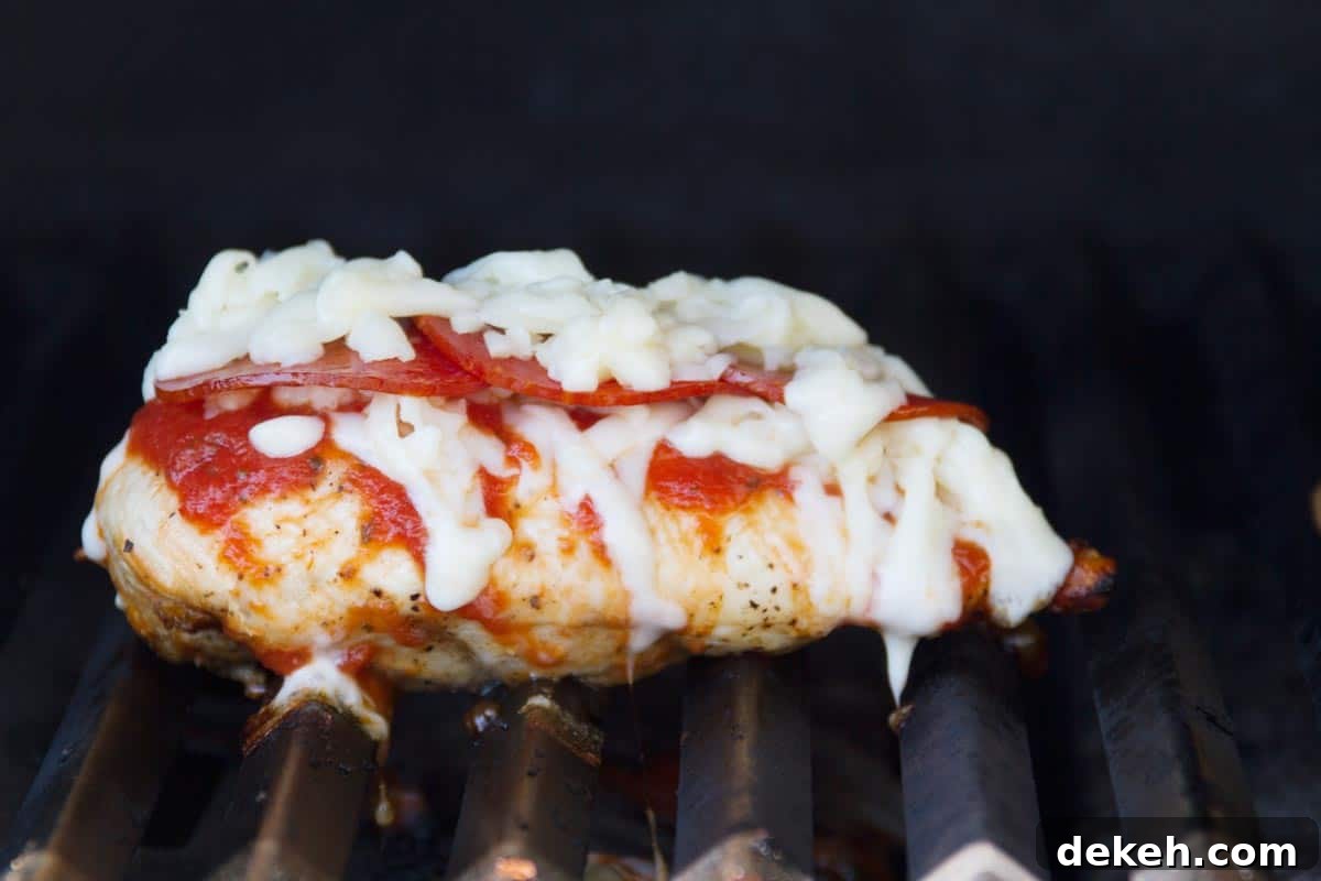 Chicken breast on a grill topped with pizza sauce, pepperoni, and cheese