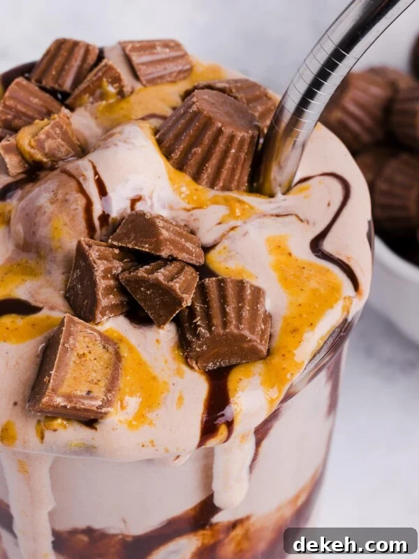 A close up shot of a Ninja Creami milkshake topped with peanut butter cups and drizzled with peanut butter and chocolate sauce.