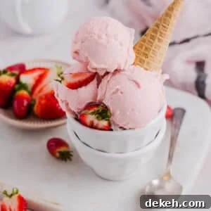 Scoops of strawberry ice cream in a bowl with a sugar cone.
