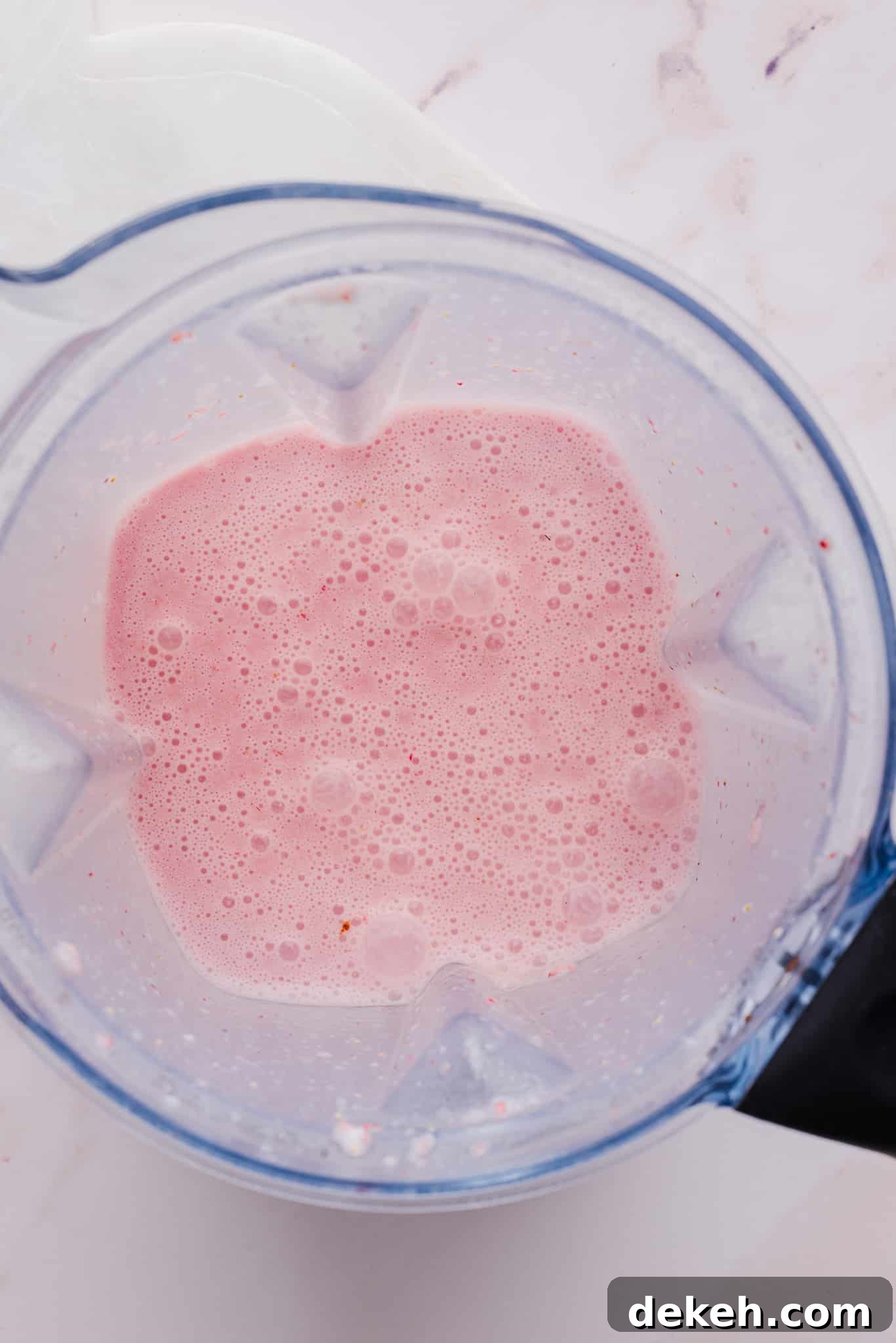 Ingredients for strawberry ice cream blended together in a blender.