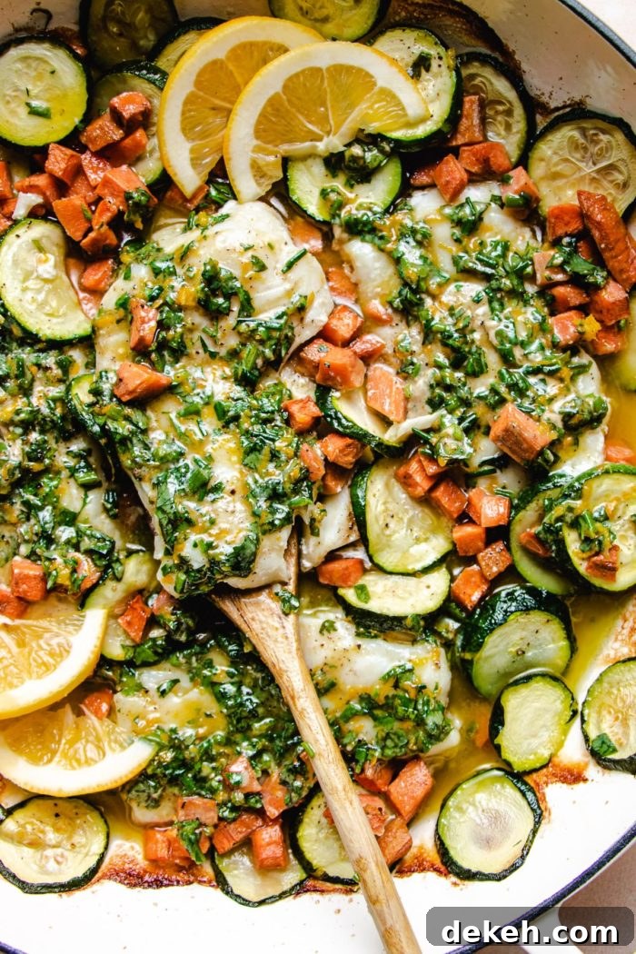 An overhead close shot photo shows the baked fish cod with melted herb butter, vegetables, and sliced lemon wedges in one pan