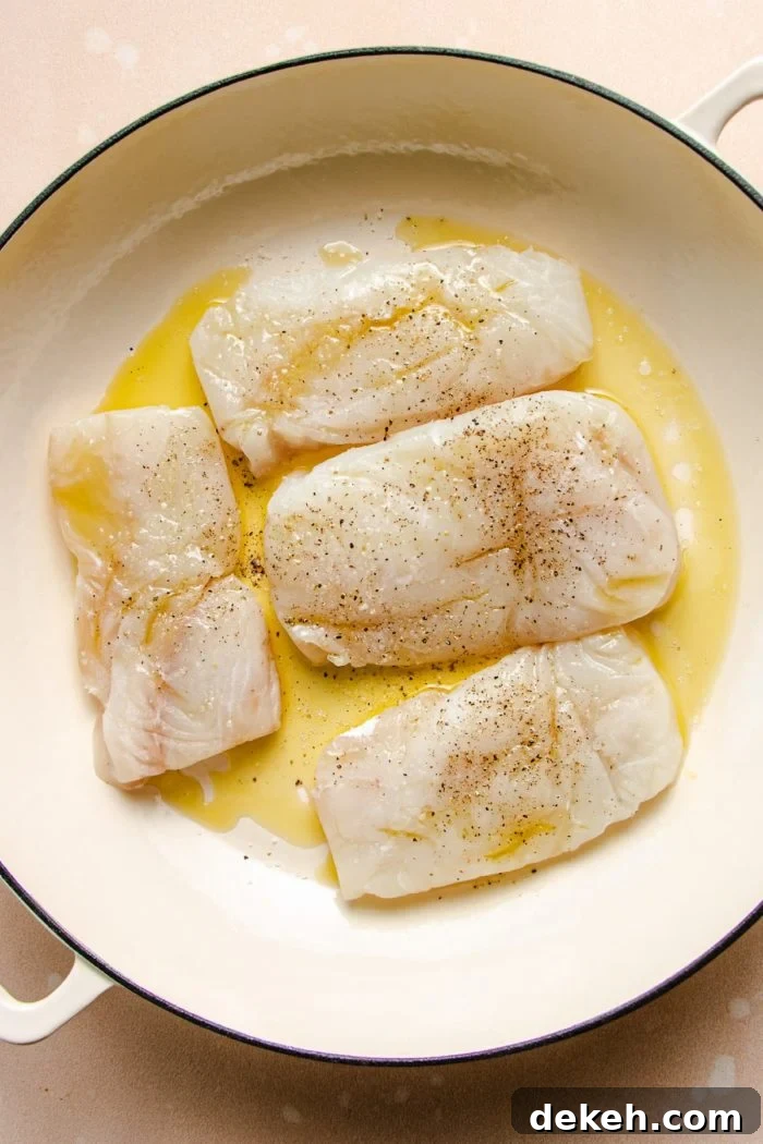 Photo shows 4 cod fillets seasoned and placed in a large casserole skillet