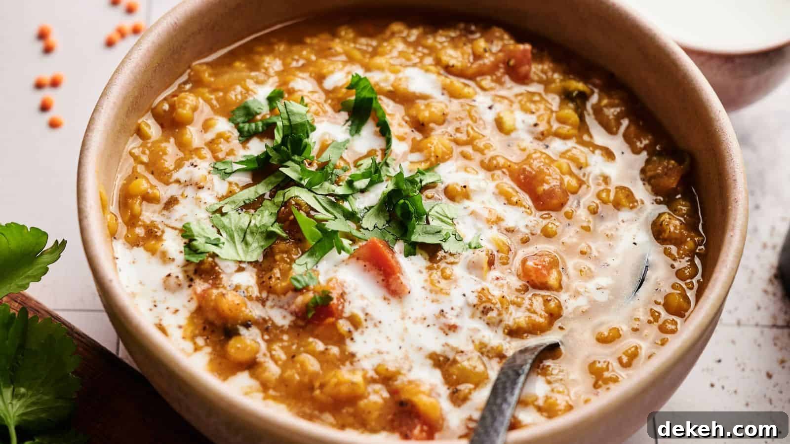 A bowl of lentil curry garnished with chopped cilantro and a swirl of cream, with a spoon in the bowl.