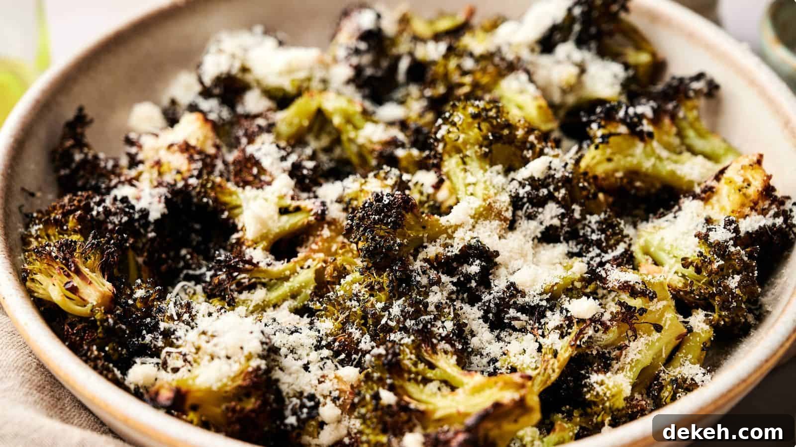 A bowl of roasted broccoli topped with grated cheese and seasoning.