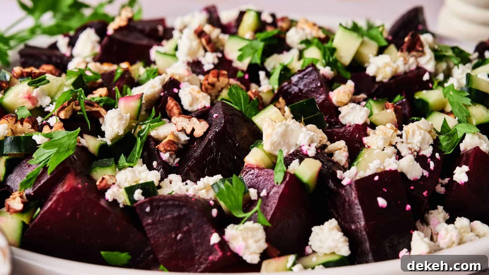 A close-up of a salad featuring chopped beets, cucumber, feta cheese, walnuts, and fresh herbs on a white plate.