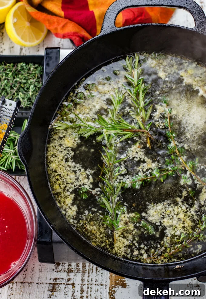 Thyme, Rosemary and garlic simmers in white wine in a black cast iron skillet. A red and orange napkin, small bowls of thyme and rosemary and a bowl of blood orange juice sit next to the skillet.