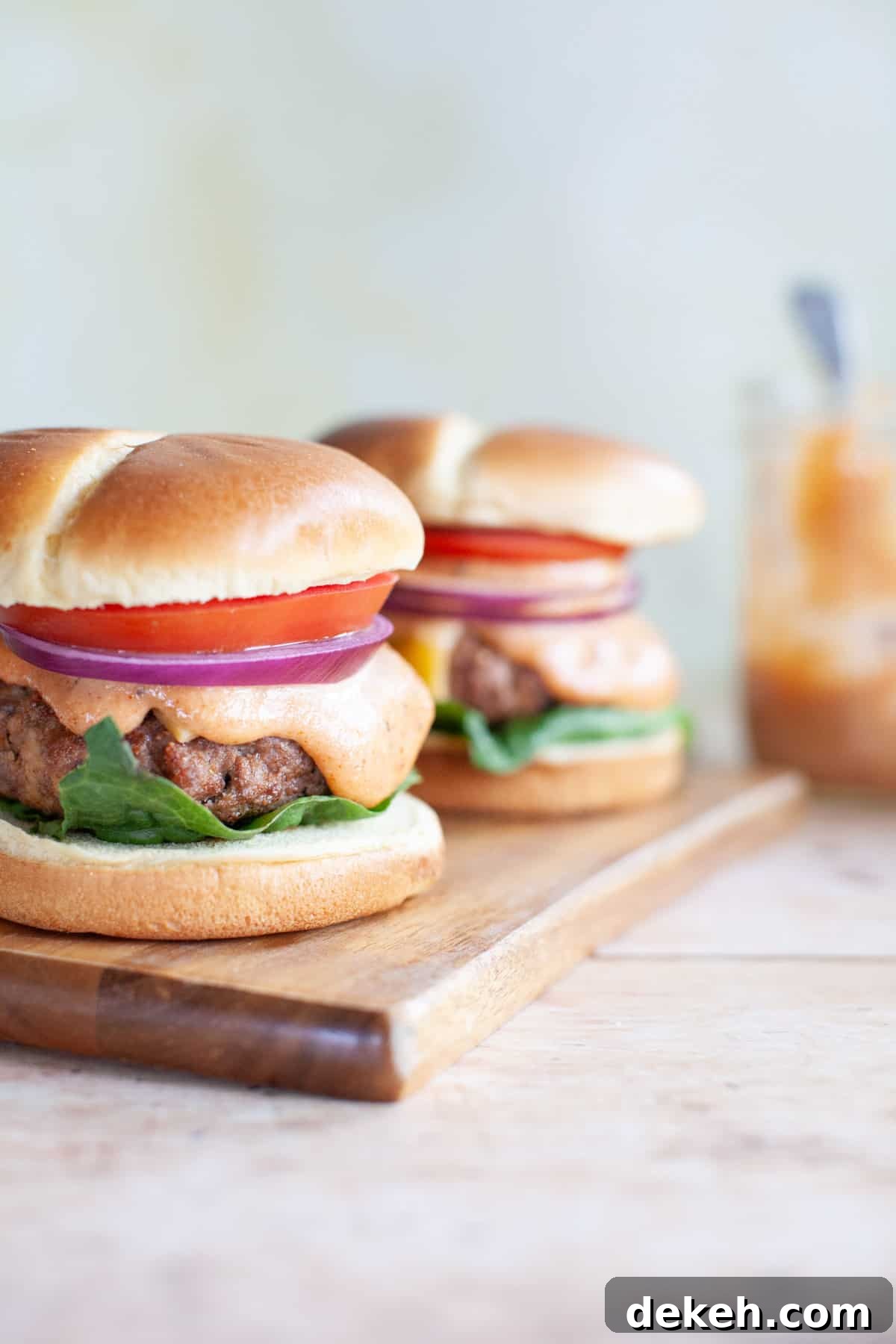 two beef burgers all the way on buns sitting on a wood board