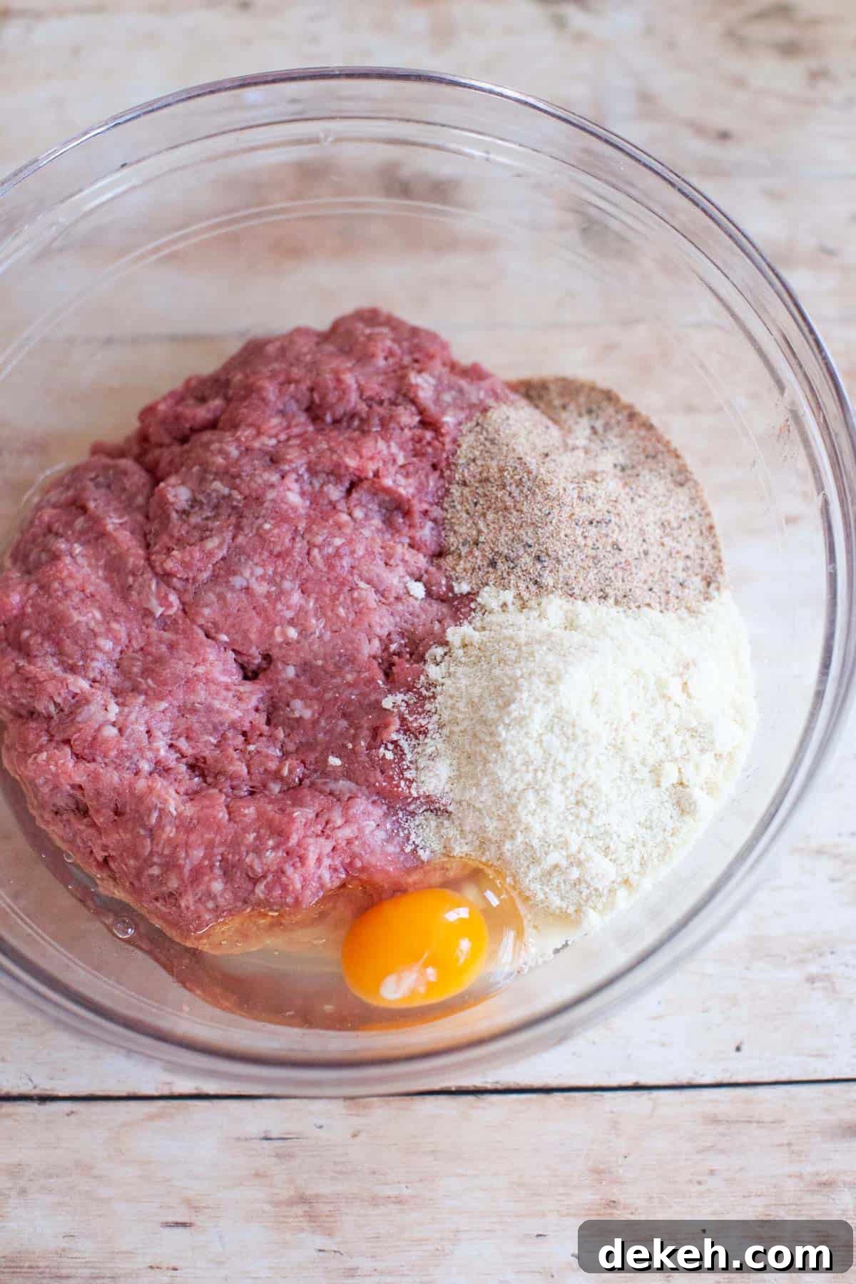 Ground beef with beef burger seasoning, almond flour, and egg in a glass mixing bowl.