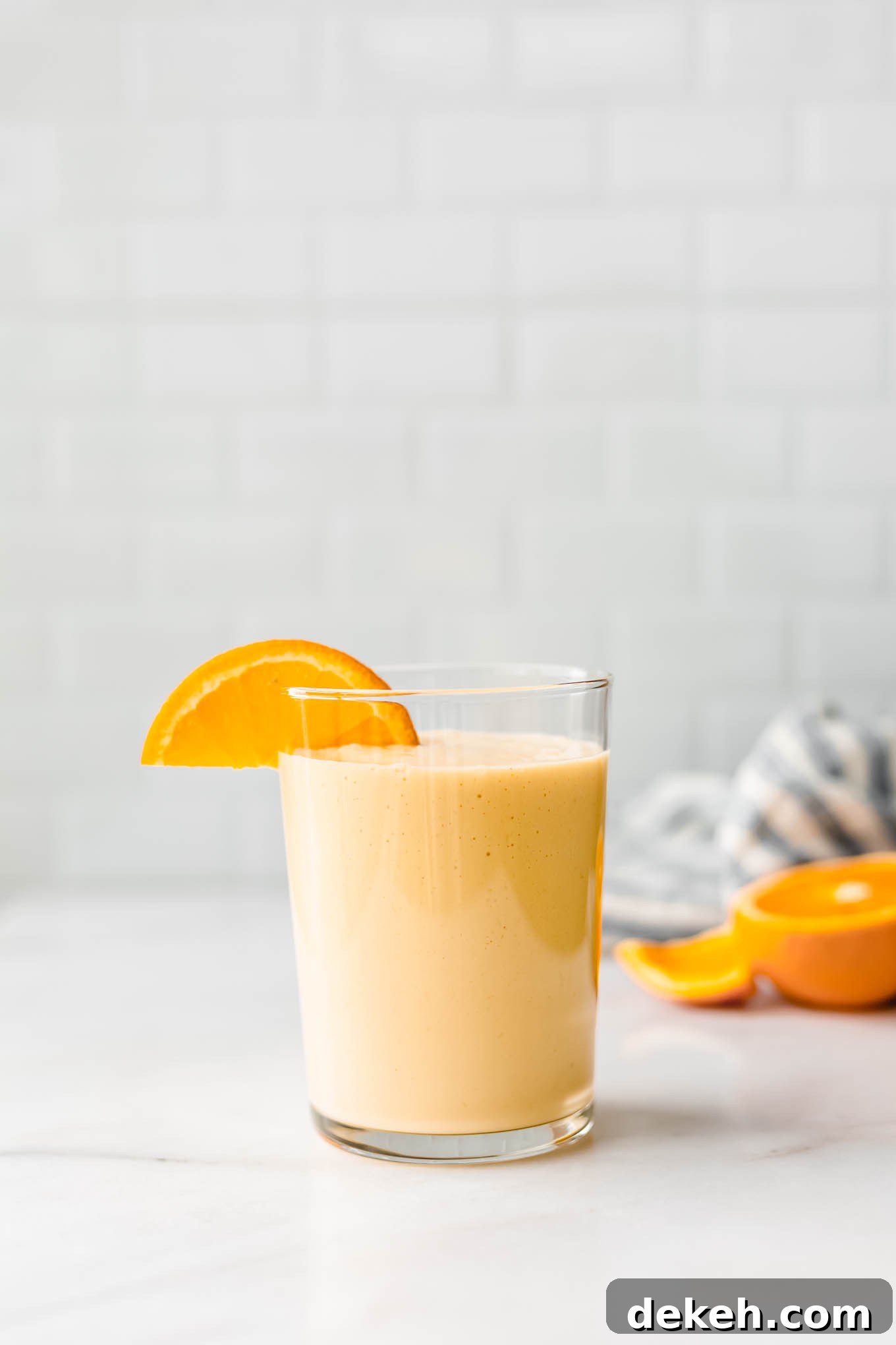 an orange smoothie on a white marble counter with a blue striped napkin