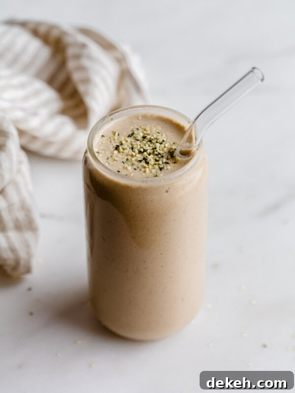 A banana date smoothie in a glass topped with hemp seeds and a striped beige napkin on the side.