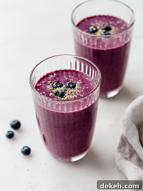 Two glasses of blueberry spinach smoothie topped with hemp seeds and blueberries