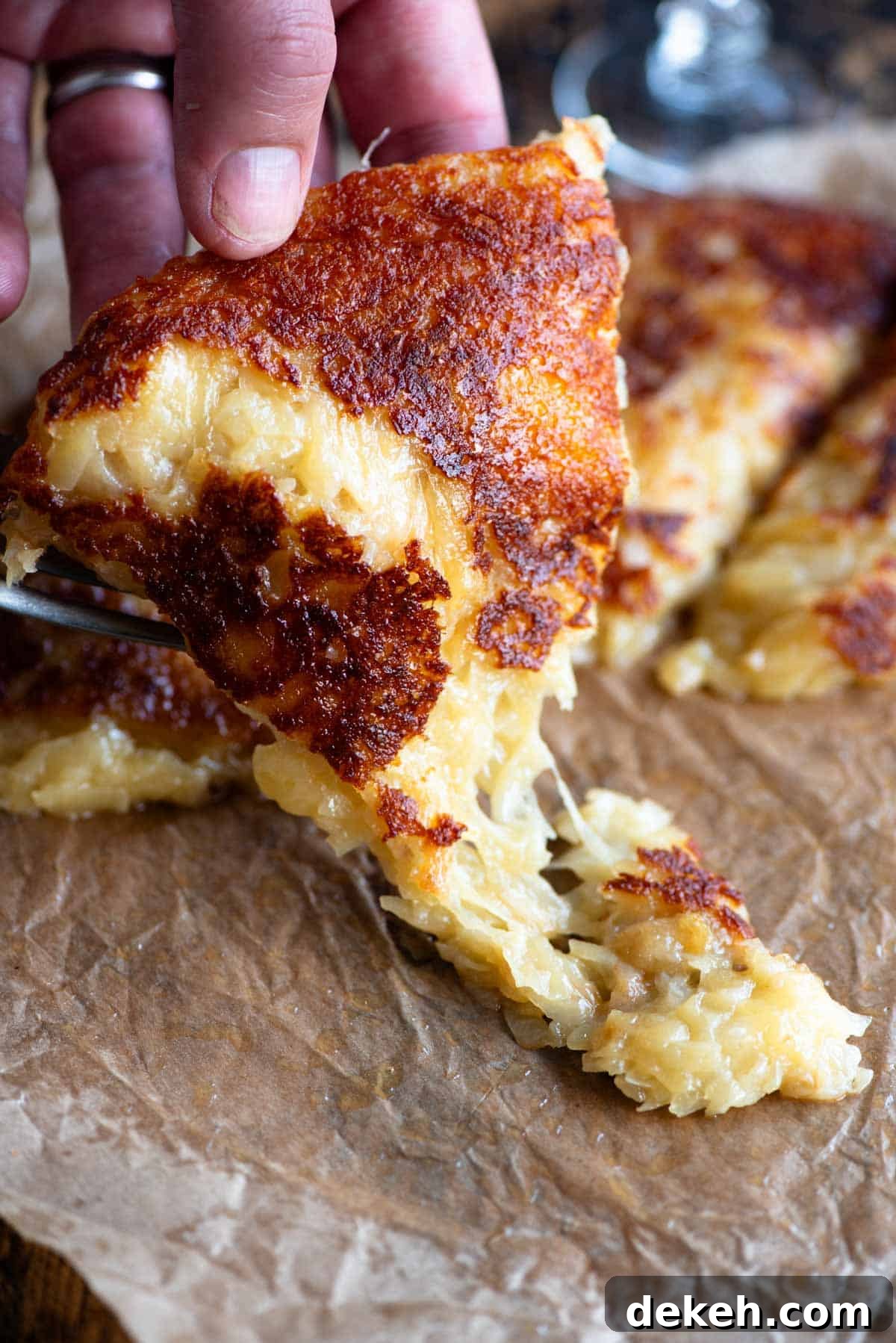 A hand picking up a slice of fried cheese and potato (frico) from a wooden board.