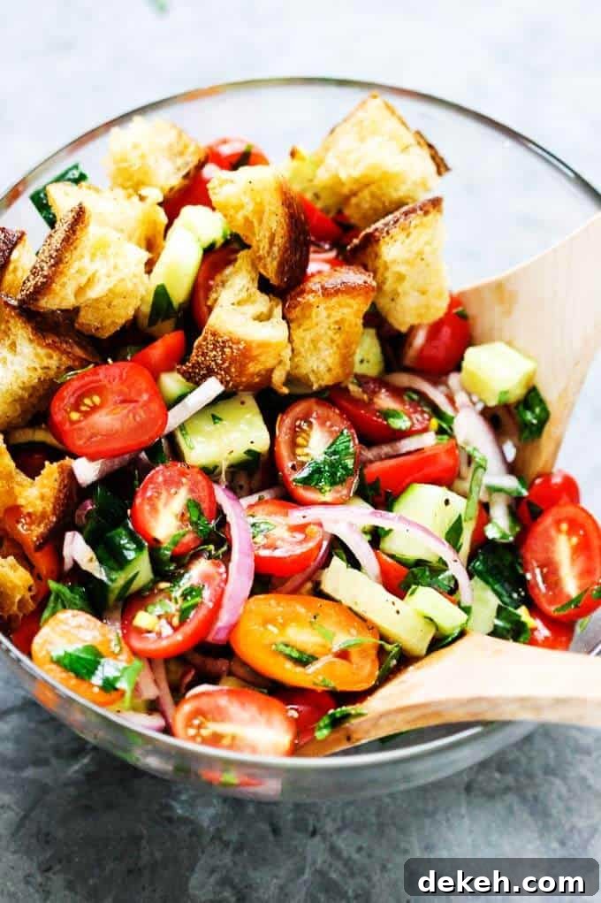 Panzanella Salad in a glass bowl with two wooden spoons.