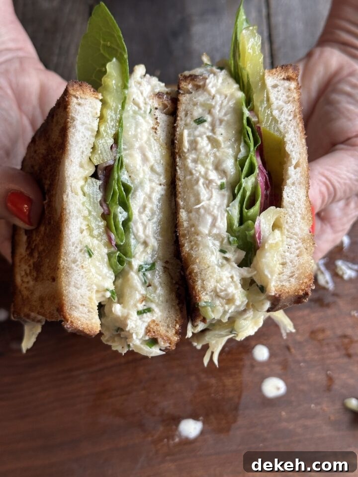 Teri holding a cut grilled chicken salad sandwich with pickles, romaine lettuce, and marinated onions over a wooden board