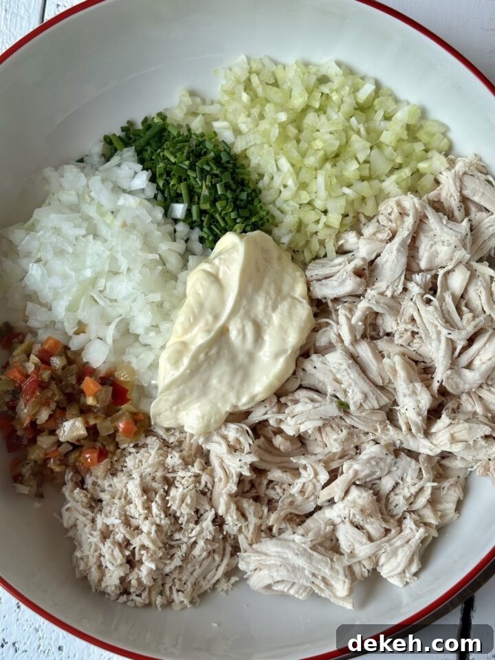 ingredients for a chicken salad in white mixing bowl with a red rim