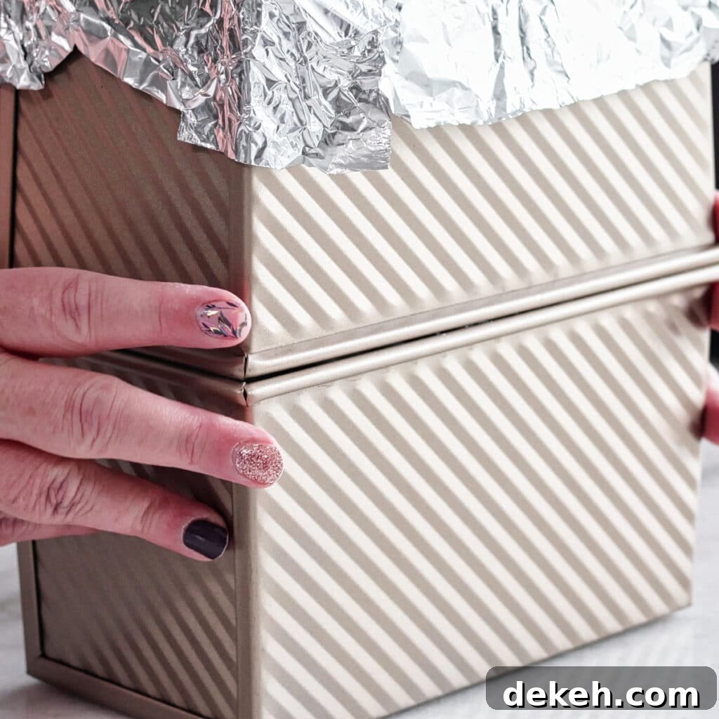 placing another loaf pan with foil on it on top of loaf pan with bread in it.