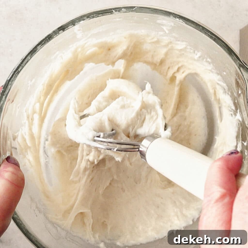 using a Danish dough whisk to deflate the dough in the glass bowl.