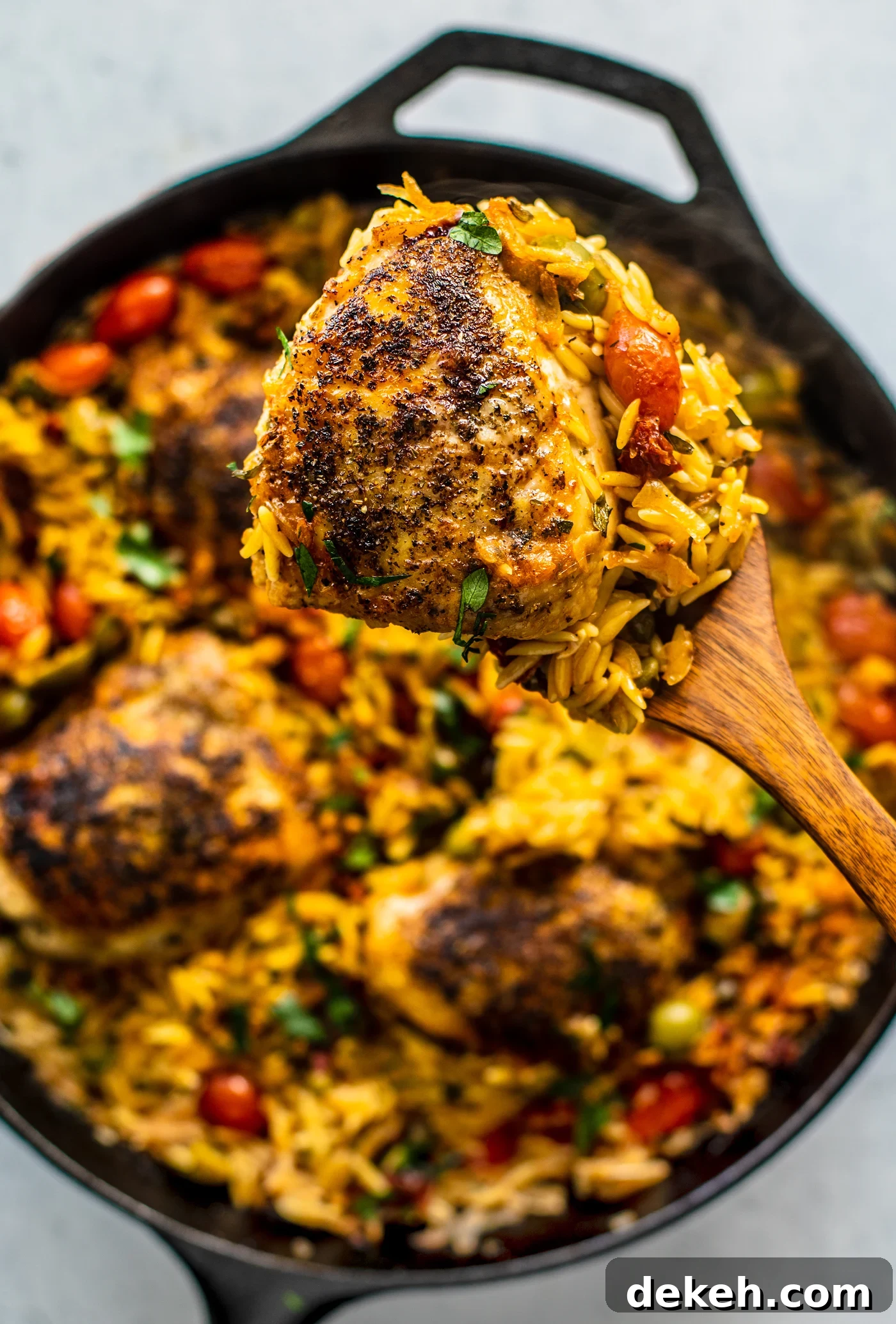 Spatula lifting a portion of chicken out of the skillet full or orzo.