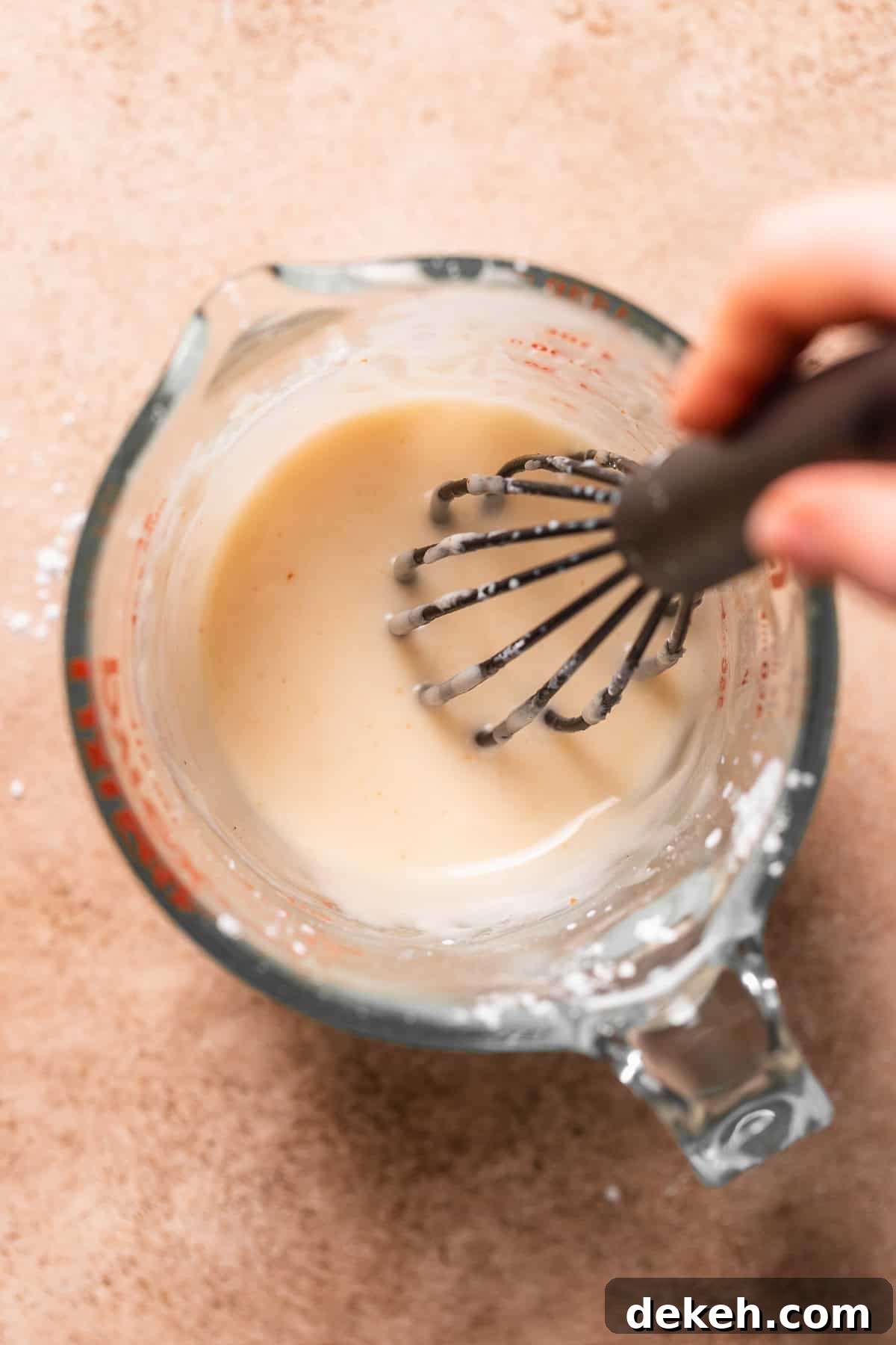 A hand whisking the brown butter glaze in a measuring glass.