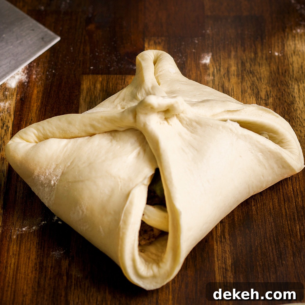 A square of bread dough filled with cooked cabbage and ground beef with the corners folded over to create a pocket.