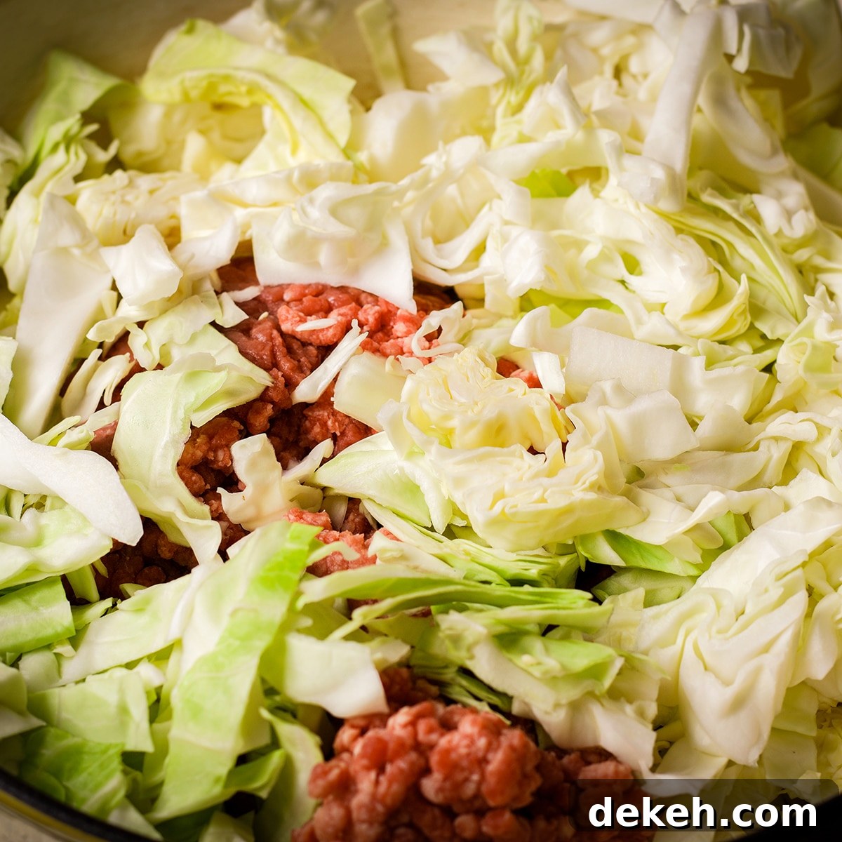 Ground beef and chopped cabbage cooking in a saucepan.