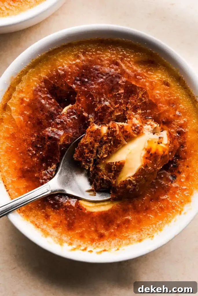 Close-up of a spoon lifting a bite of pumpkin creme brulee, showcasing the creamy texture beneath the crisp caramelized sugar.
