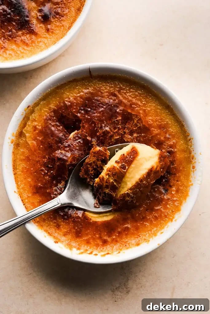 Spoon breaking into the caramelized top of pumpkin creme brulee, revealing the smooth custard layer below.