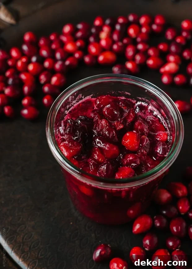 A jar of cranberry sauce surrounded by cranberries.