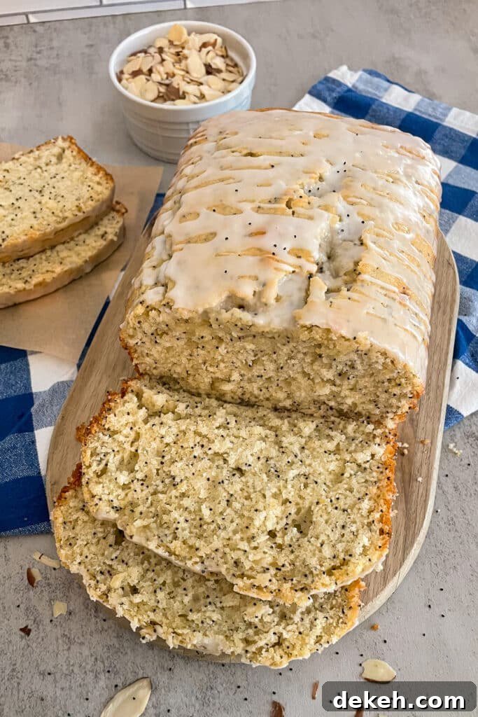 loaf of easy almond poppyseed bread shown on a cutting board with slices for serving and a bowl of sliced almonds