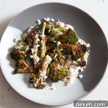 Charred broccoli with calabrian chili, feta, and lemon yogurt sauce on a gray and white plate.