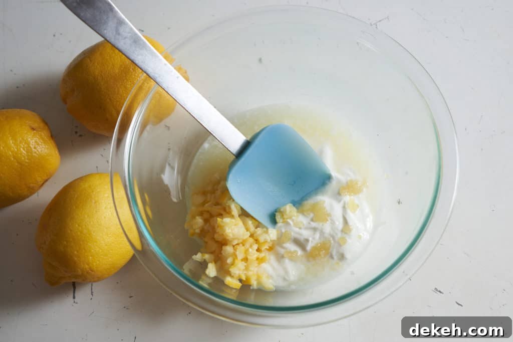 Lemon juice and pieces of lemon peel being stirred into yogurt in a bowl.