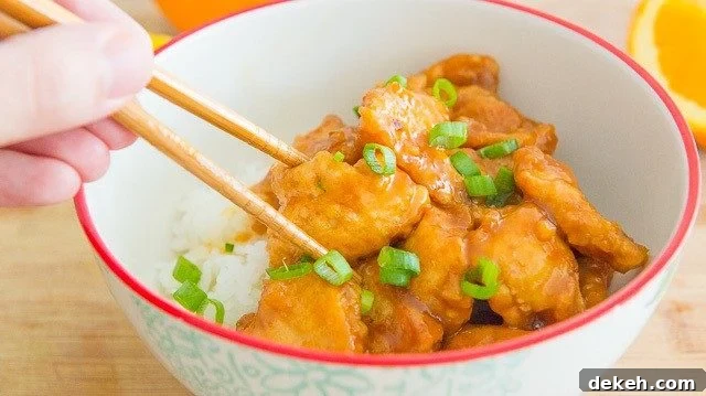 Chopstick Holding a Piece of Orange Chicken in a Bowl