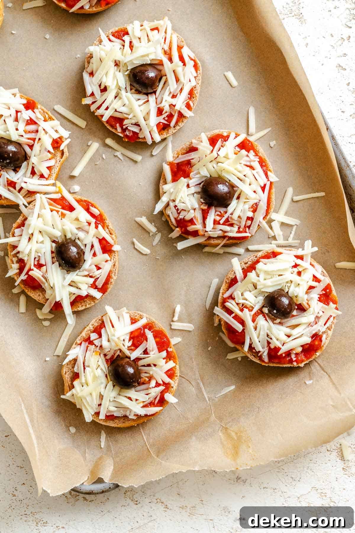 Process shots showing adding olives to mini spider pizzas.
