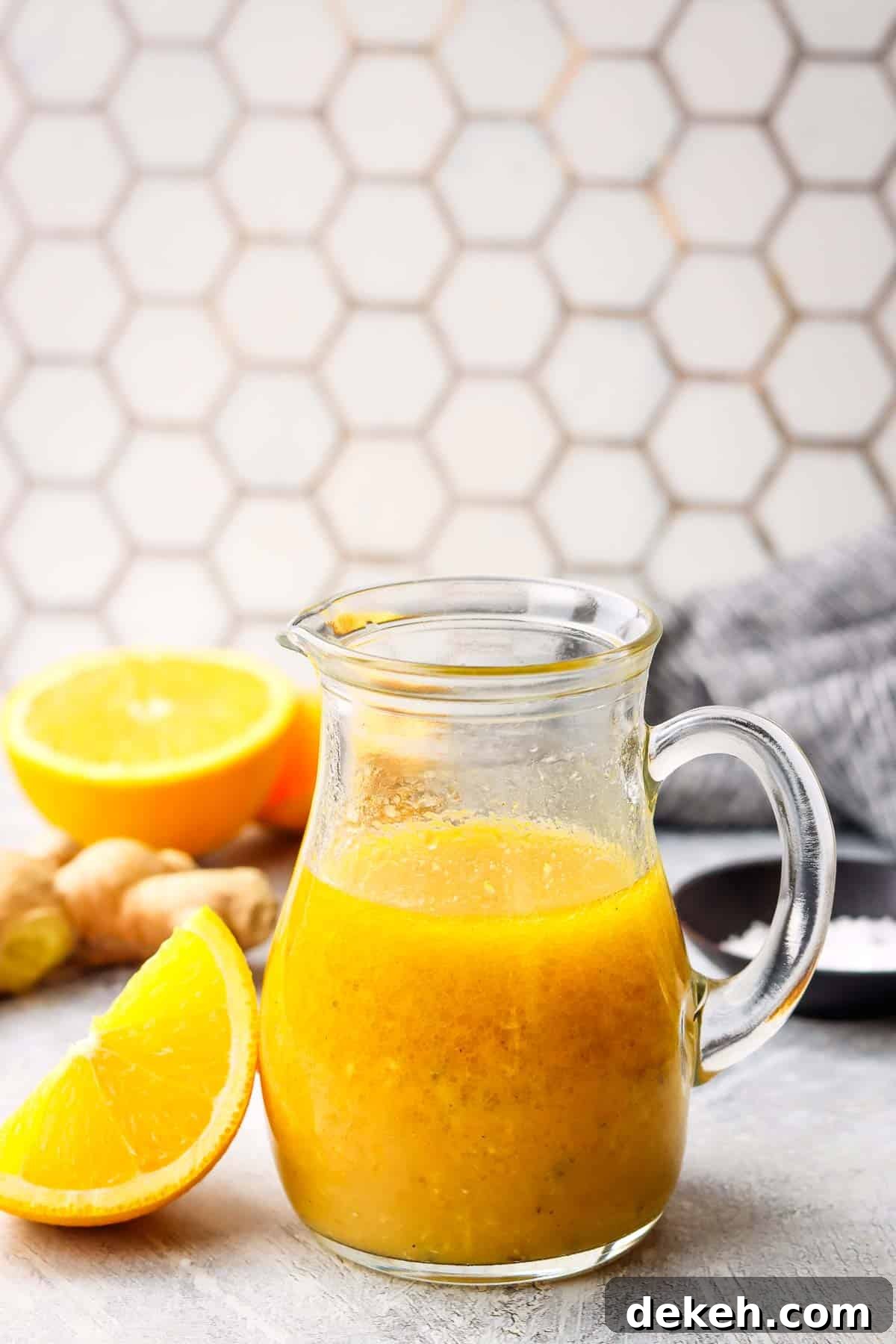 a small jug with orange ginger dressing and fresh oranges and ginger in the background.