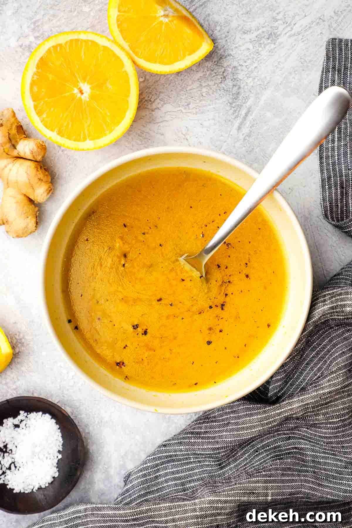 A bowl of ginger orange ginger dressing with a whisk in it and an orange half and ginger root in the background.