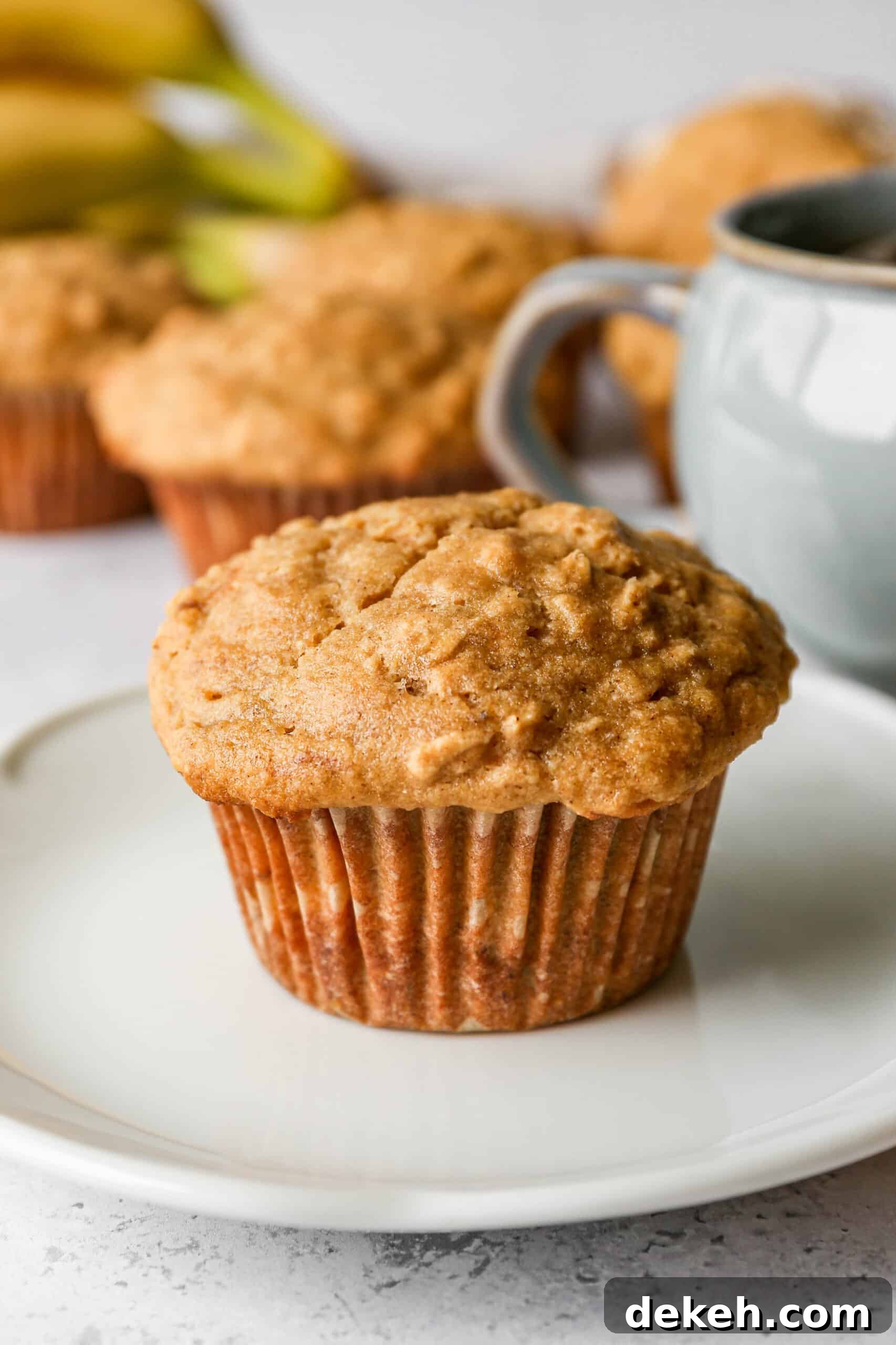 a gluten free banana oat muffin on a white plate next to a mug of tea.