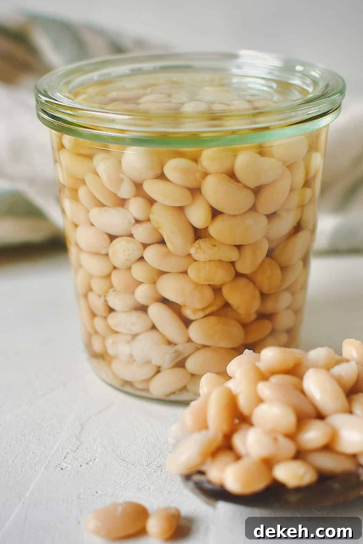 Cooked beans, stored in a glass jar for later use. some laying in a spoon on the table on the side of the jar.
