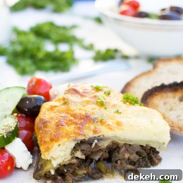 A piece of easy moussaka on a white plate with bread and Greek salad