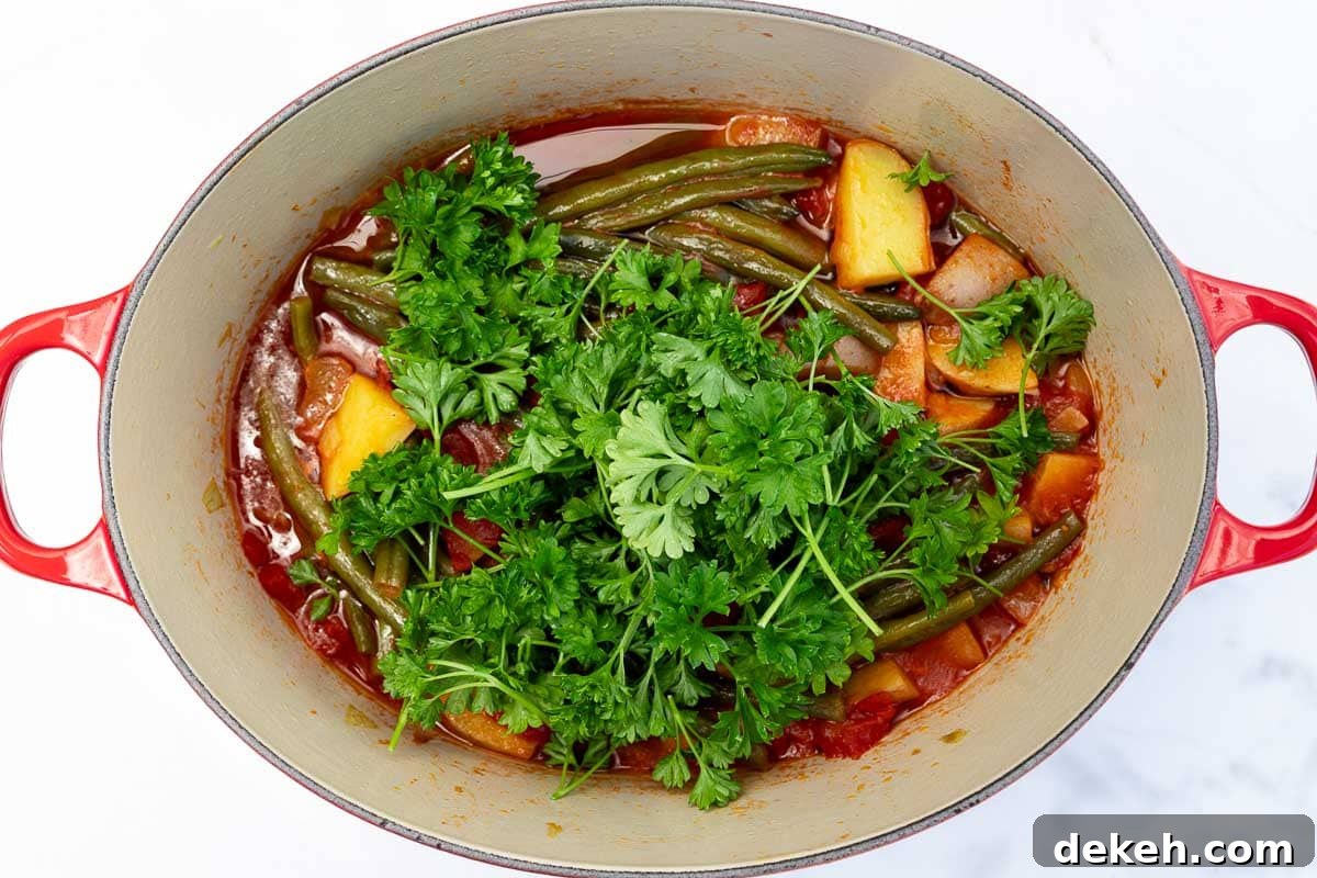 Overhead image of a red cast iron pot with a Greek green bean stew in it, with fresh parsley on top ready to be mixed in.