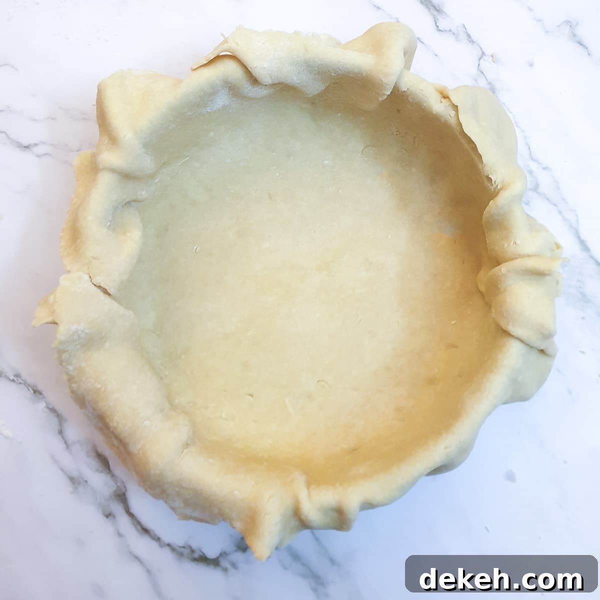 A round baking dish lined with pastry, with the pastry overhanging the edges of the dish.