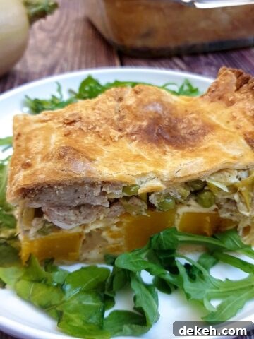 A slice of butternut, leek and sausage pie on a white plate.