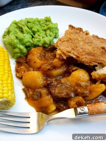 A helping of meat and potato pie on a plate with vegetables.